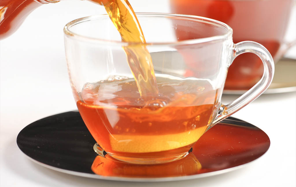 rooibos tea being poured into a clear glass cup