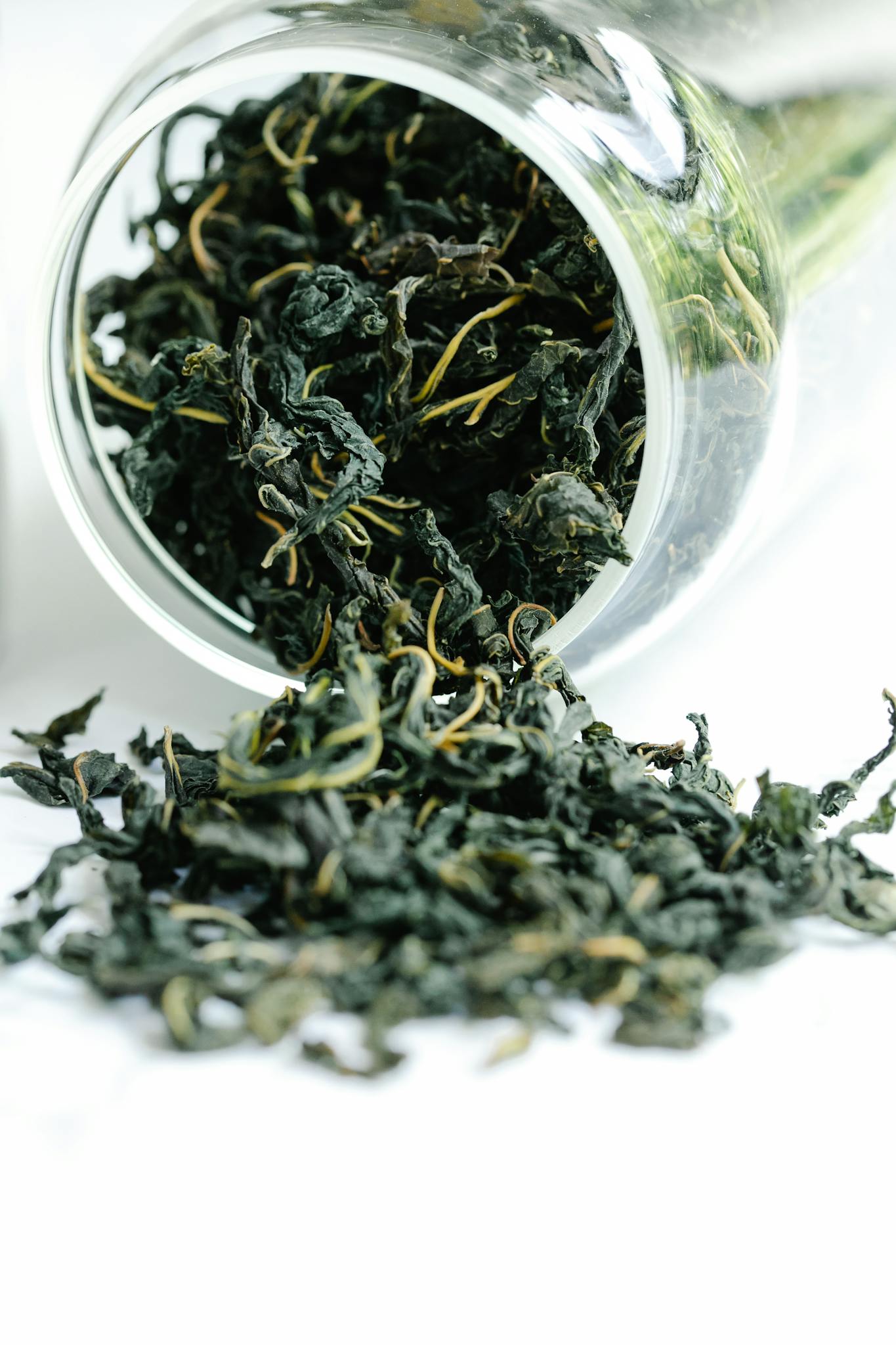 A close-up of dried black tea leaves spilling from a glass jar, showcasing texture and freshness.